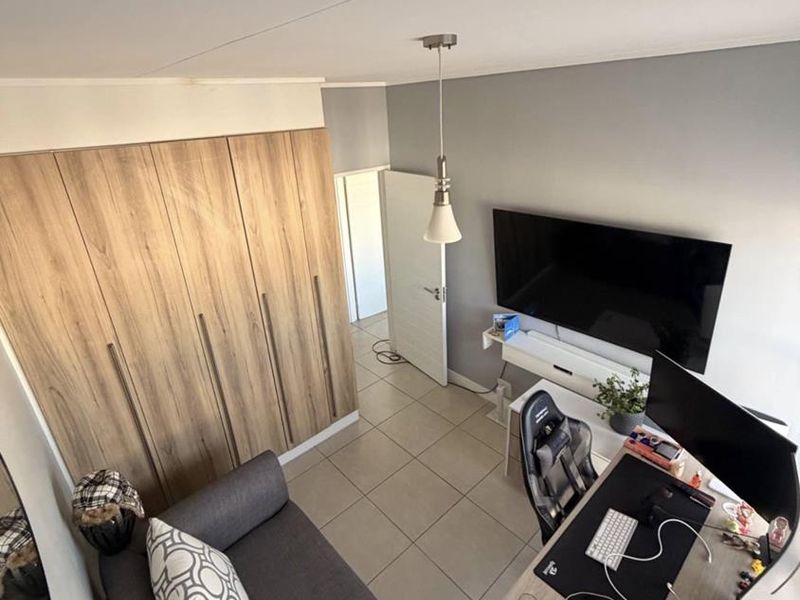 A well-maintained bedroom featuring modern wood-finish built-in wardrobes, neutral tiled flooring, and a contemporary pendant light fixture.