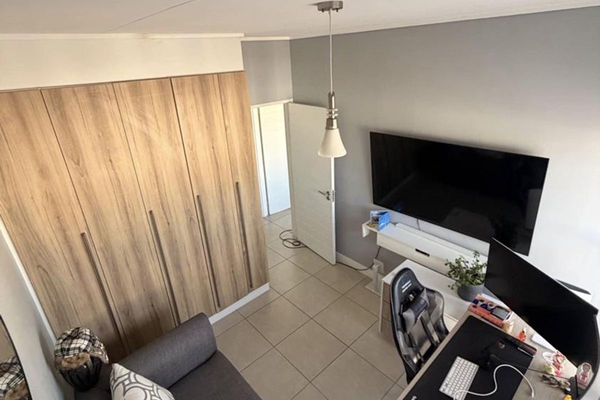 A well-maintained bedroom featuring modern wood-finish built-in wardrobes, neutral tiled flooring, and a contemporary pendant light fixture.