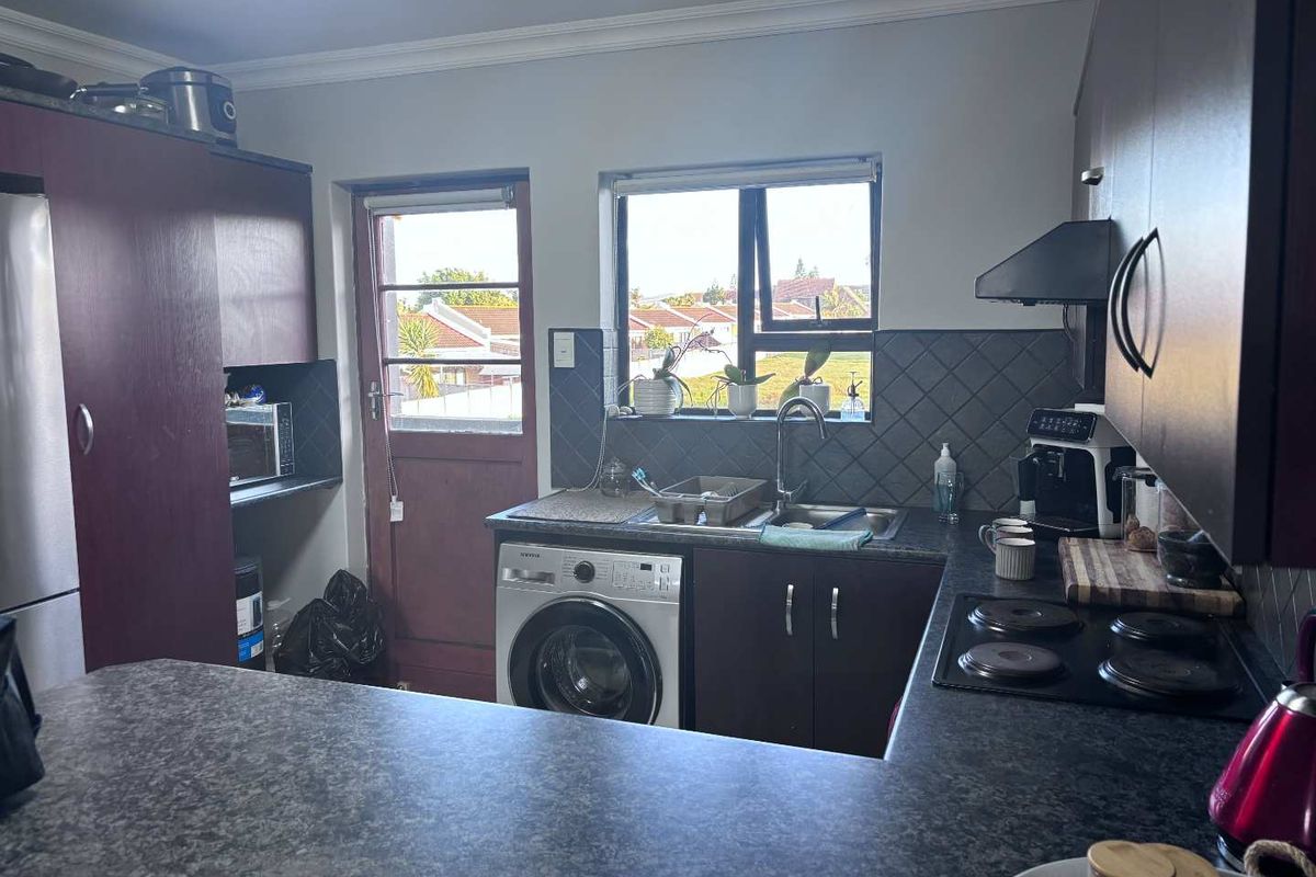 Functional kitchen featuring dark cabinetry, laminate countertops, integrated electric hob, extractor fan, and space for a washing machine with direct exterior access.