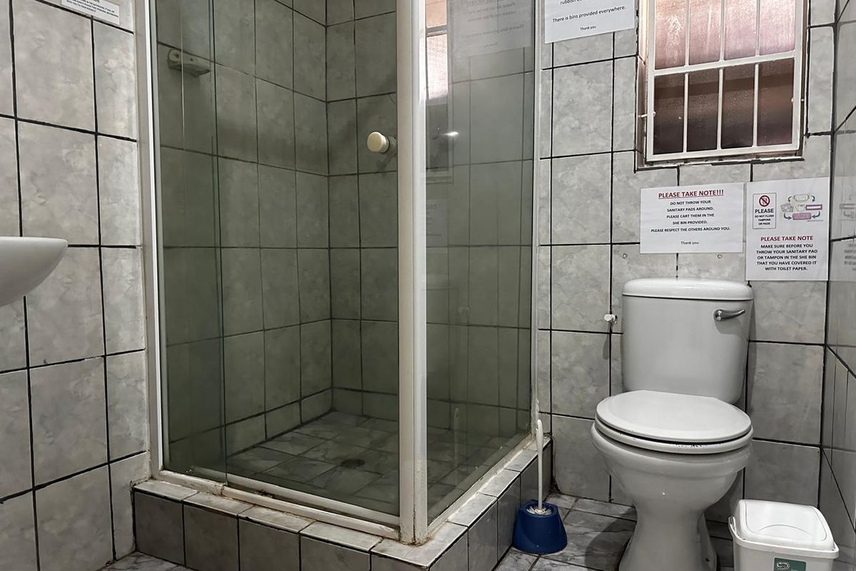 A compact bathroom featuring a corner shower enclosure, a standard toilet, and tiled walls and flooring throughout.