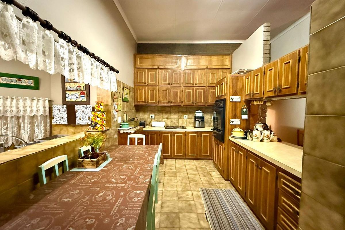 A traditional kitchen featuring extensive wooden cabinetry, built-in oven, tiled countertops, and a breakfast bar area with a connected dining space.