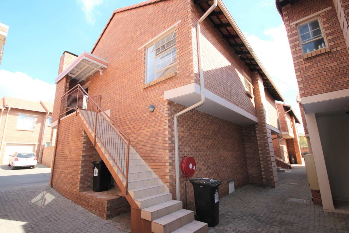 Exterior view of a face brick apartment building featuring an external staircase, paved courtyard area, and functional fire safety equipment.
