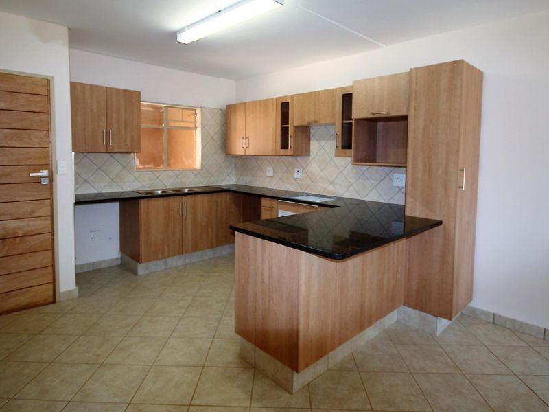 A functional kitchen featuring laminate cabinetry, granite countertops, a double basin sink, and tiled flooring in an open-plan layout.