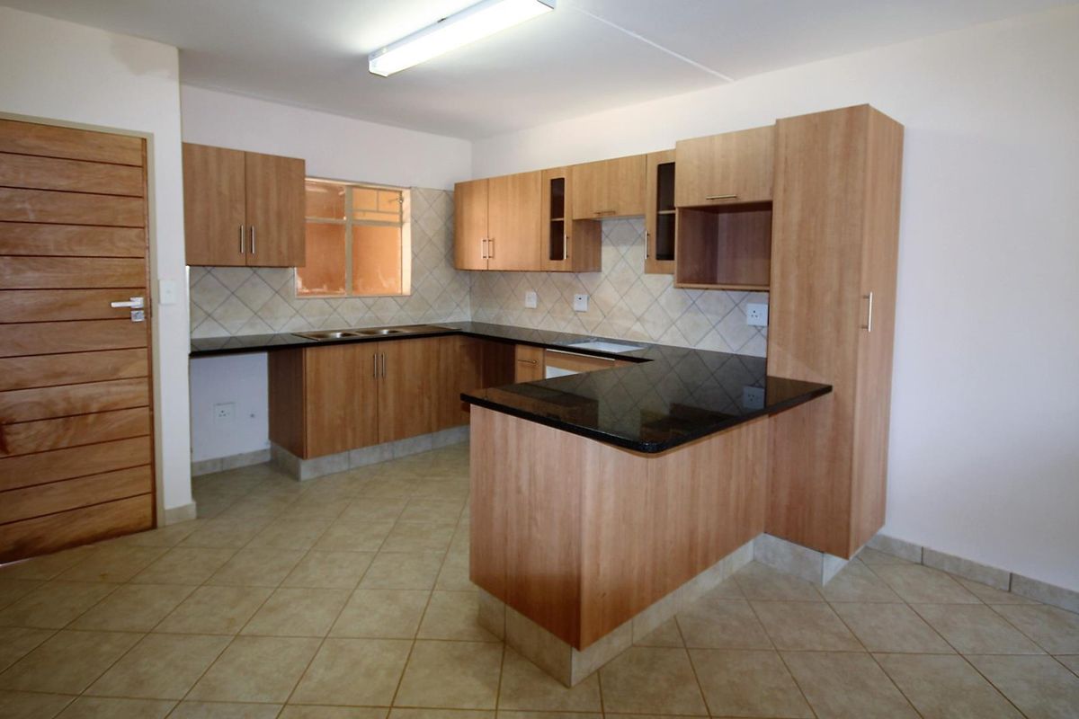 A functional kitchen featuring laminate cabinetry, granite countertops, a double basin sink, and tiled flooring in an open-plan layout.