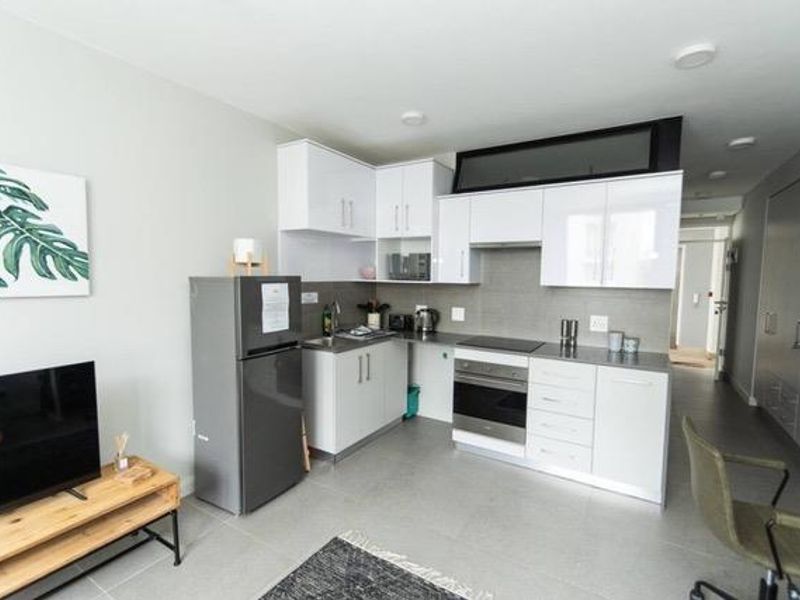 Modern open-plan apartment featuring a sleek kitchen with white cabinetry, integrated appliances, and tiled flooring, seamlessly flowing into the living area.