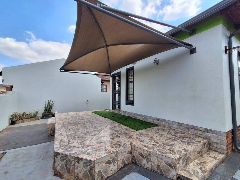 A paved outdoor patio area featuring a modern shade sail, security gate access, and artificial grass detailing, providing a functional exterior space.
