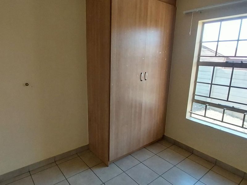 A simple bedroom featuring tiled flooring, a built-in wardrobe, and a window with security bars.
