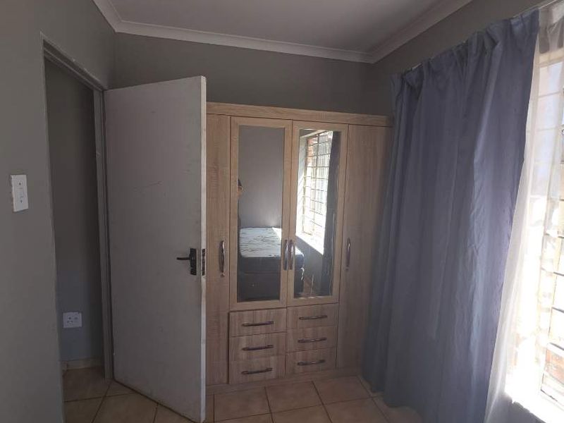 A bedroom featuring tiled flooring, a built-in wardrobe with mirrored panels, and a window fitted with security bars.