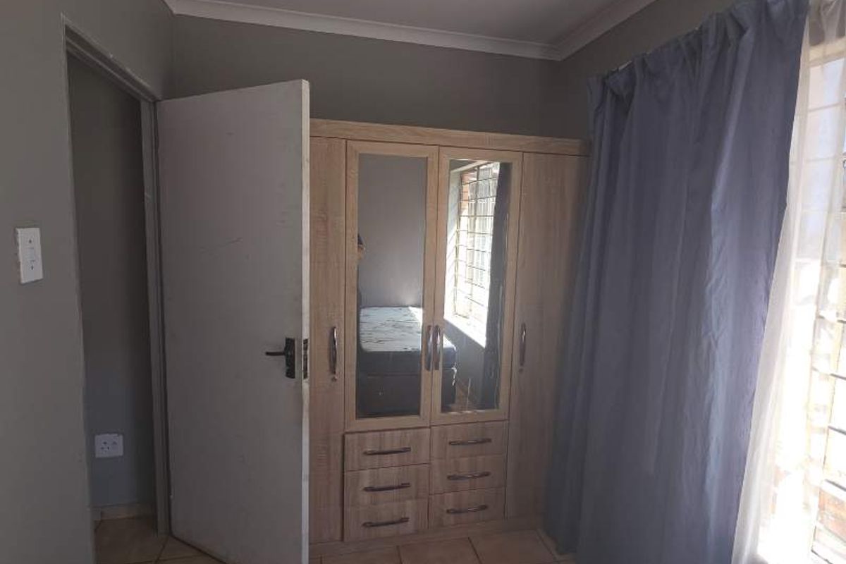 A bedroom featuring tiled flooring, a built-in wardrobe with mirrored panels, and a window fitted with security bars.