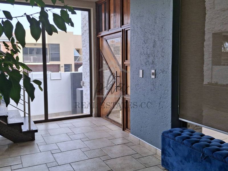 Modern entrance hall featuring a striking timber-framed glass door, textured feature wall, and stone tile flooring with access to an adjacent staircase.