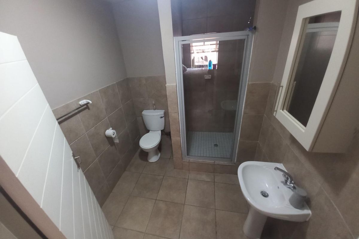 A functional bathroom featuring a pedestal basin, a toilet, and a glass-enclosed shower with neutral wall and floor tiling.