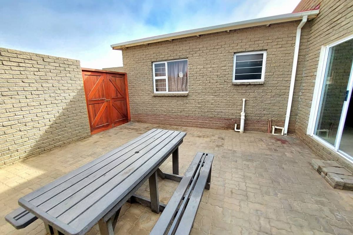 A paved rear courtyard area featuring brick wall construction, a wooden gate, and sliding door access to the main dwelling.