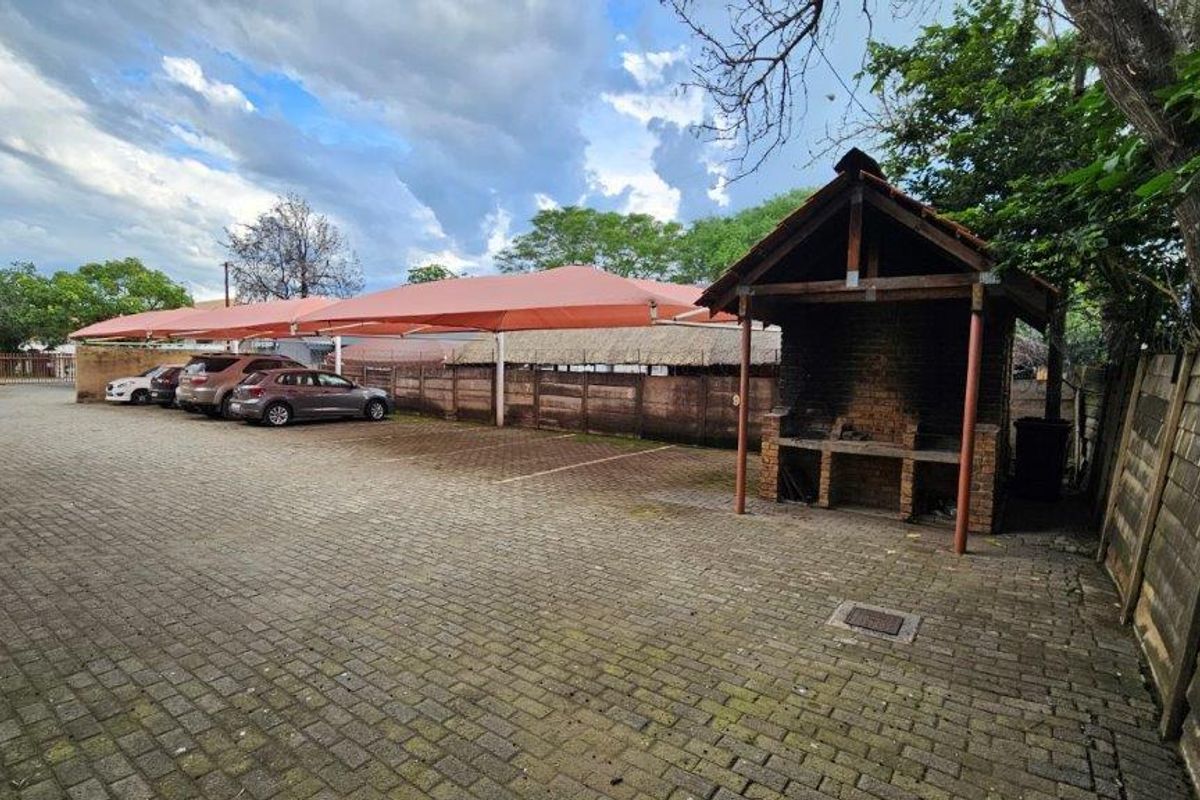 Outdoor communal area featuring paved parking bays with shade cloth carports and a built-in brick braai facility.