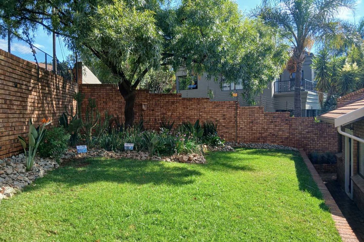 A well-maintained rear garden featuring a manicured lawn, established trees, and a perimeter brick boundary wall.