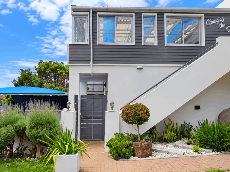 Rear elevation of a multi-level home featuring a paved patio area, external staircase, and modern sliding glass doors leading to the interior.