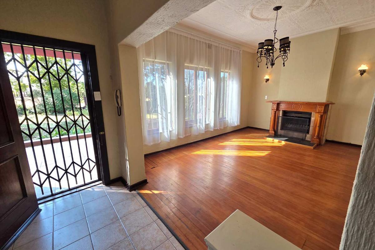 Spacious living room featuring original wooden flooring, a classic fireplace with mantel, and an ornate ceiling rose, leading to a tiled entrance area.
