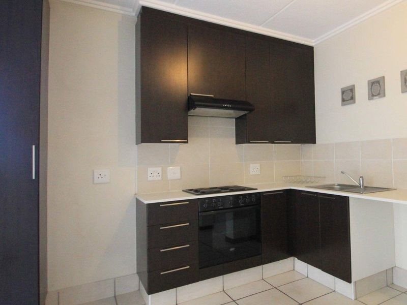 A clean, functional kitchen featuring dark cabinetry, built-in oven with gas hob, extractor fan, and neutral tiled flooring and backsplash.