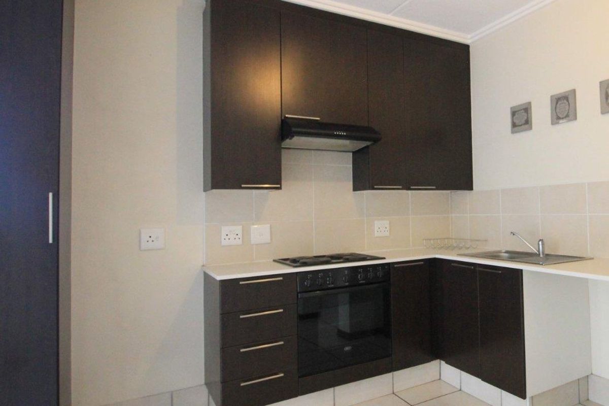 A clean, functional kitchen featuring dark cabinetry, built-in oven with gas hob, extractor fan, and neutral tiled flooring and backsplash.