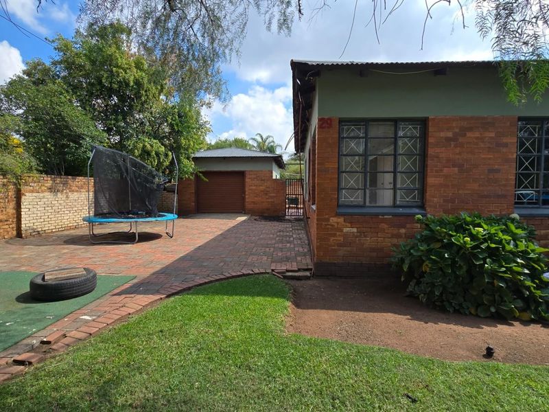 Rear exterior view of the property featuring a brick-paved courtyard, lawn area, and a detached garage with a secure boundary wall.