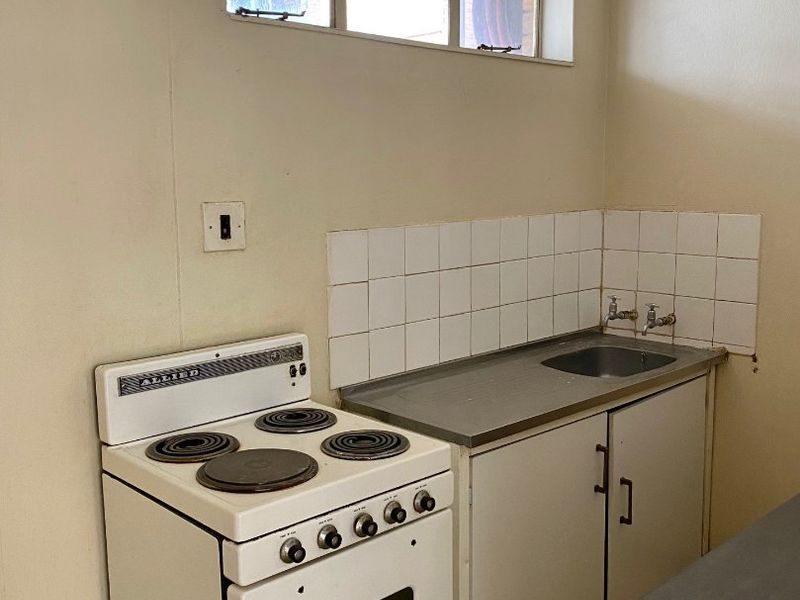 A compact, dated kitchen area featuring a stainless steel sink, tiled splashback, and a freestanding electric stove.