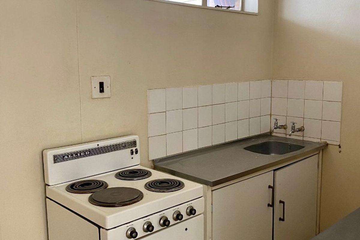 A compact, dated kitchen area featuring a stainless steel sink, tiled splashback, and a freestanding electric stove.