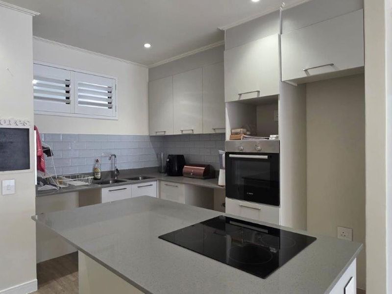 Modern kitchen featuring a central island with an integrated electric hob, sleek cabinetry, quartz countertops, and a stylish subway tile backsplash.