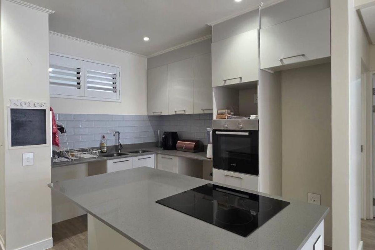 Modern kitchen featuring a central island with an integrated electric hob, sleek cabinetry, quartz countertops, and a stylish subway tile backsplash.