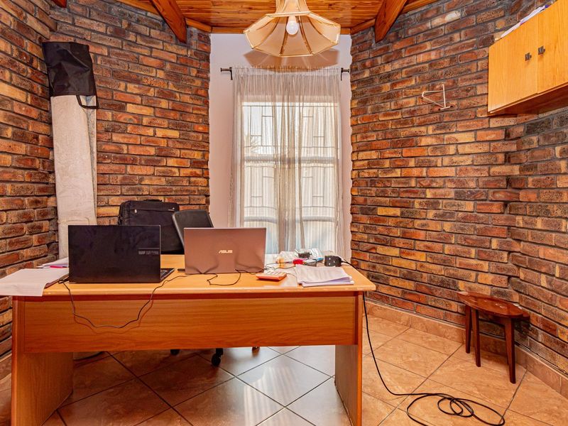A home office featuring exposed brick walls, a timber ceiling, and tiled flooring, providing a rustic and functional workspace.