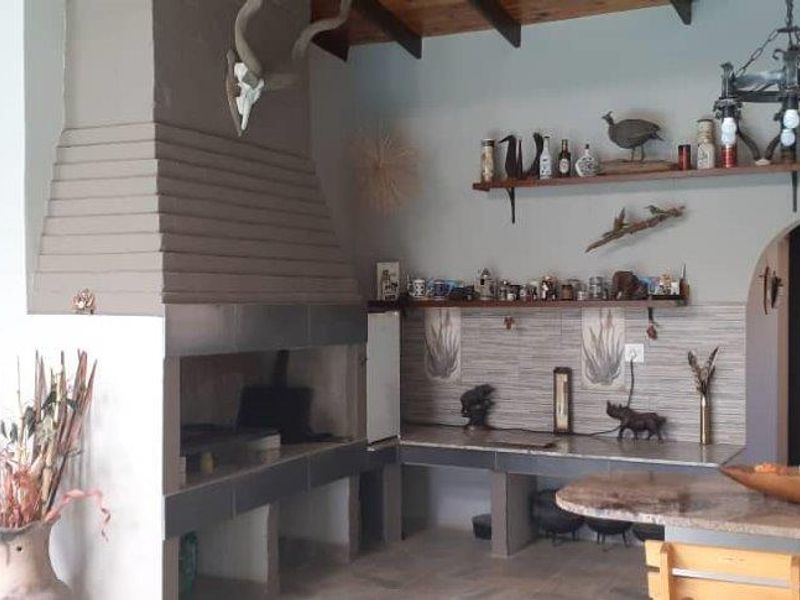 Spacious indoor entertainment area featuring a large built-in braai, tiled countertops, exposed timber ceiling beams, and an arched doorway leading to the kitchen.