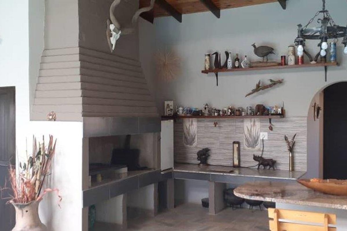 Spacious indoor entertainment area featuring a large built-in braai, tiled countertops, exposed timber ceiling beams, and an arched doorway leading to the kitchen.