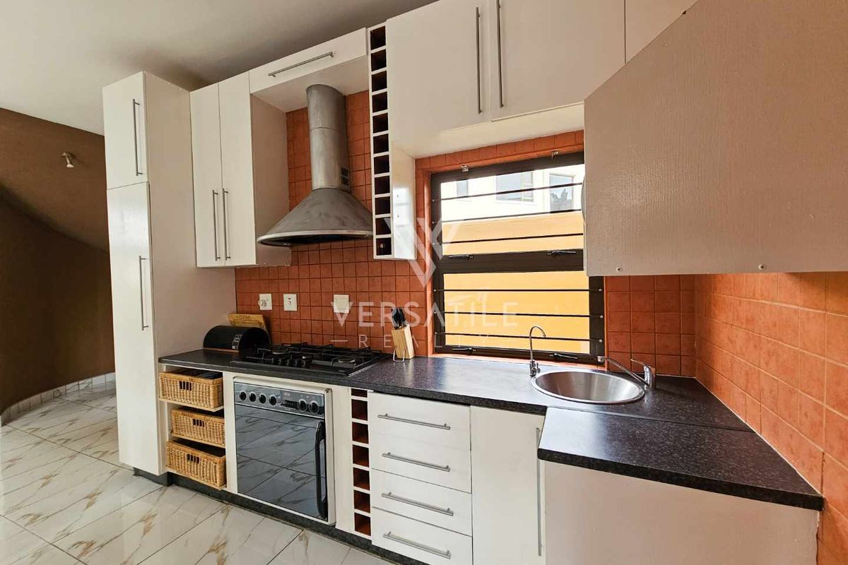 A functional kitchen featuring white cabinetry, a built-in oven with gas hob, stainless steel extractor fan, and dark laminate countertops.