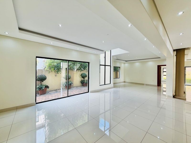 Spacious, modern open-plan living area featuring high-gloss porcelain tiles, recessed downlighting, and large sliding glass doors providing ample natural light and garden access.