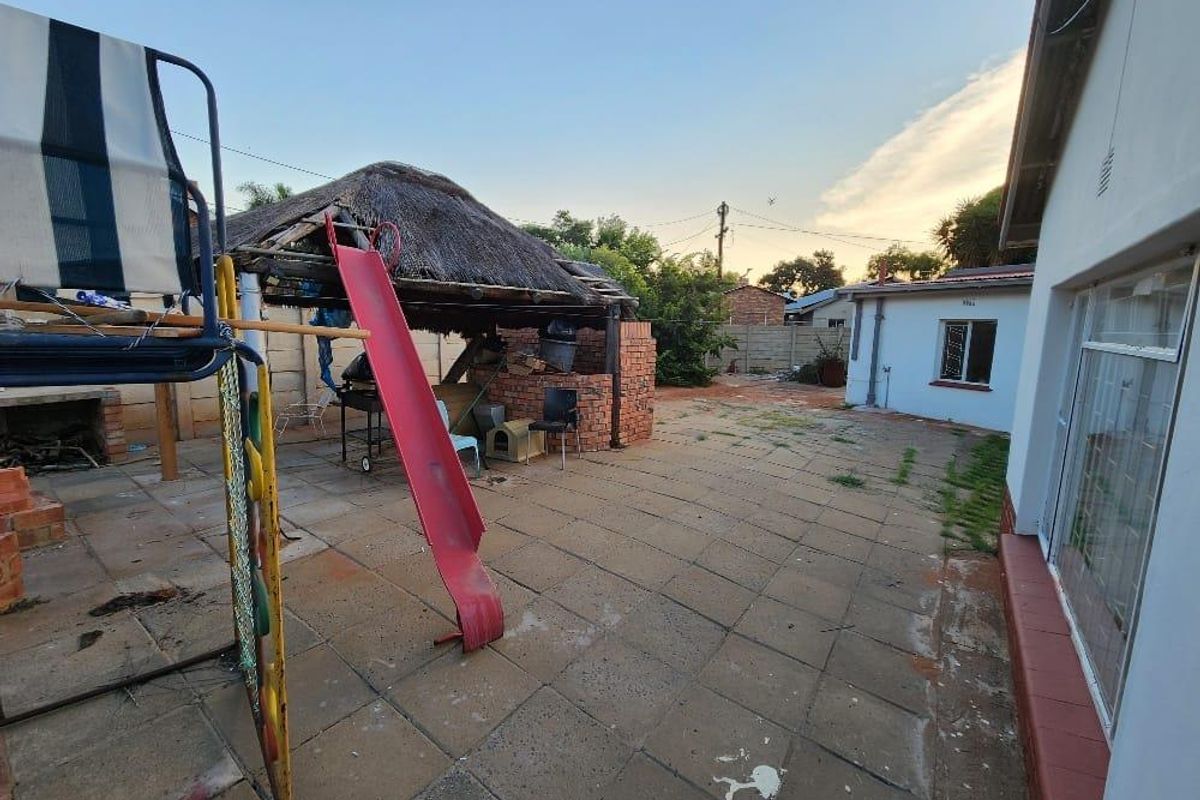 Rear exterior area featuring a paved patio, a lapa with a thatched roof, and a brick-built braai structure in a spacious backyard setting.