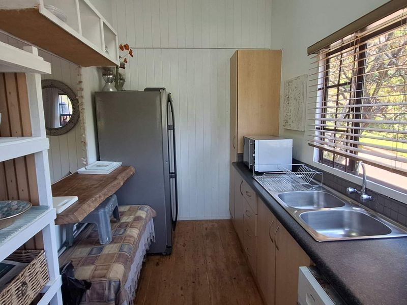 A functional kitchen featuring timber wall paneling, laminate countertops, a double bowl stainless steel sink, and timber flooring with natural light.