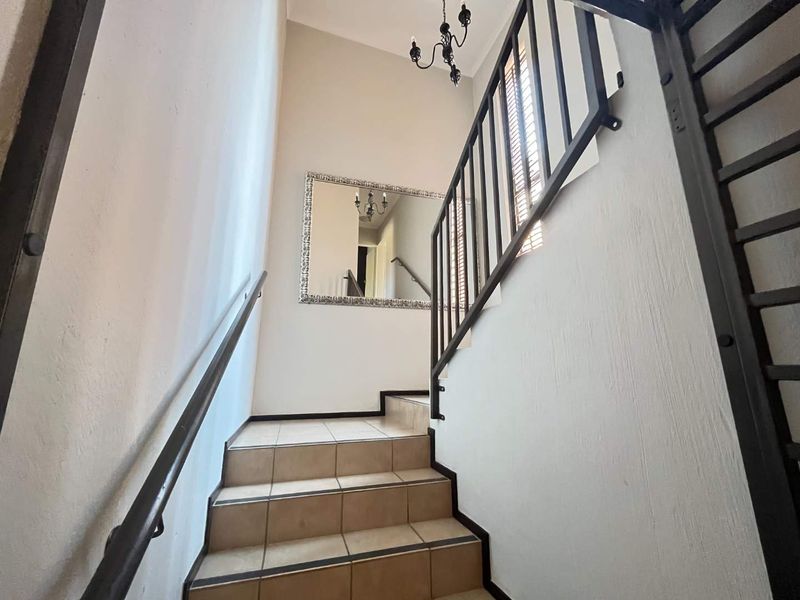 A bright staircase area featuring tiled steps, a metal balustrade, and a decorative chandelier, providing access between levels in the townhouse.