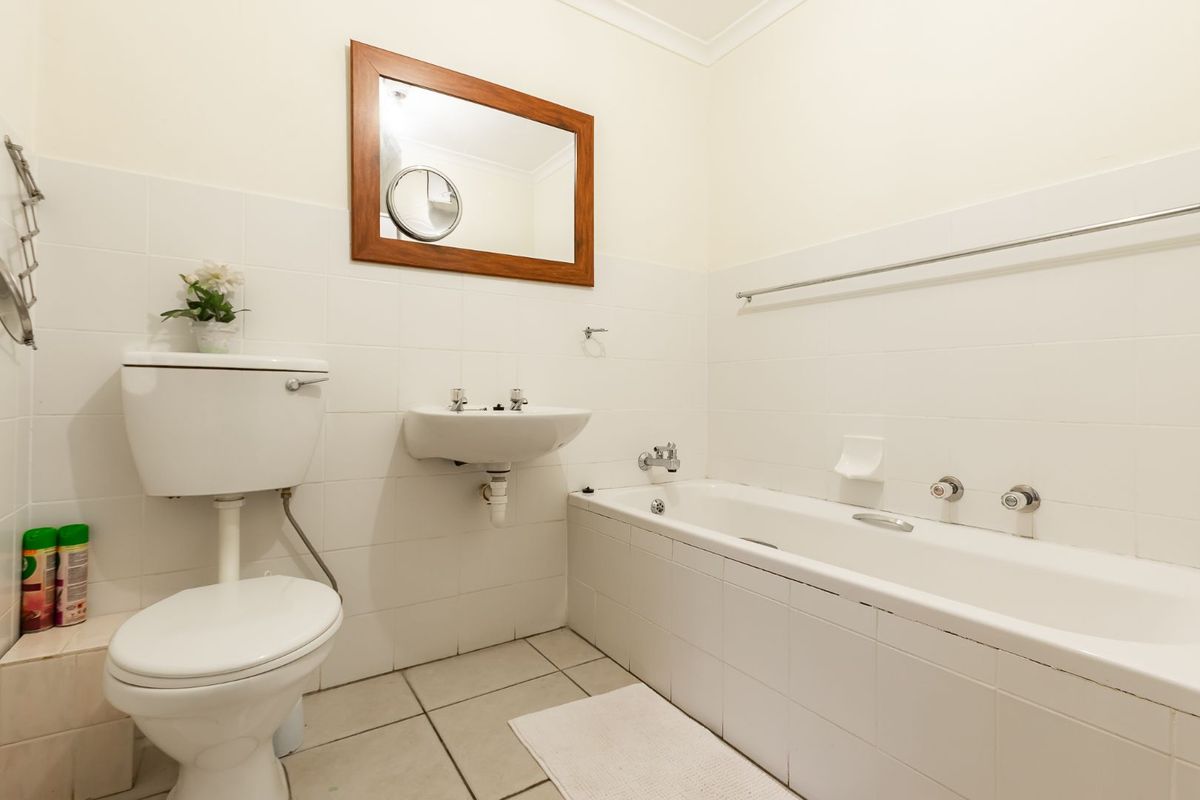 A functional bathroom featuring a white bathtub, wall-mounted basin, and toilet, finished with neutral wall tiles and floor tiling.