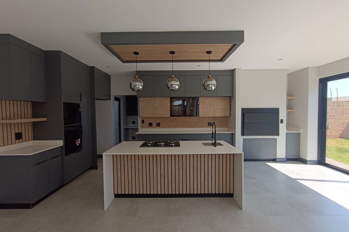 Modern kitchen featuring a central island with gas hob, sleek grey and wood cabinetry, built-in oven, and an integrated indoor braai area.