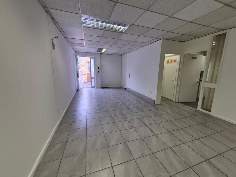 An empty office space featuring tiled flooring, a suspended ceiling with recessed lighting, and an external access door.