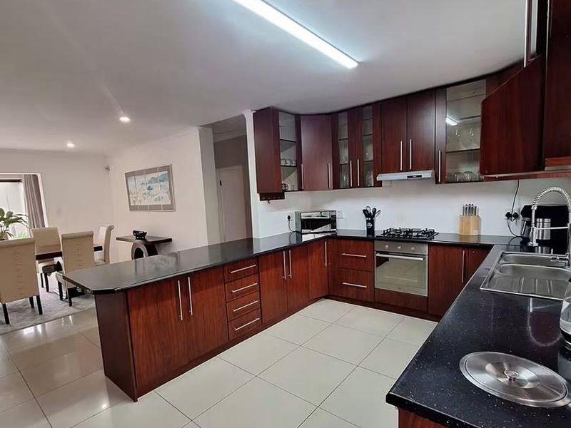 Spacious open-plan kitchen featuring dark wood cabinetry, black granite countertops, built-in appliances, and polished porcelain floor tiles, seamlessly flowing into the dining area.