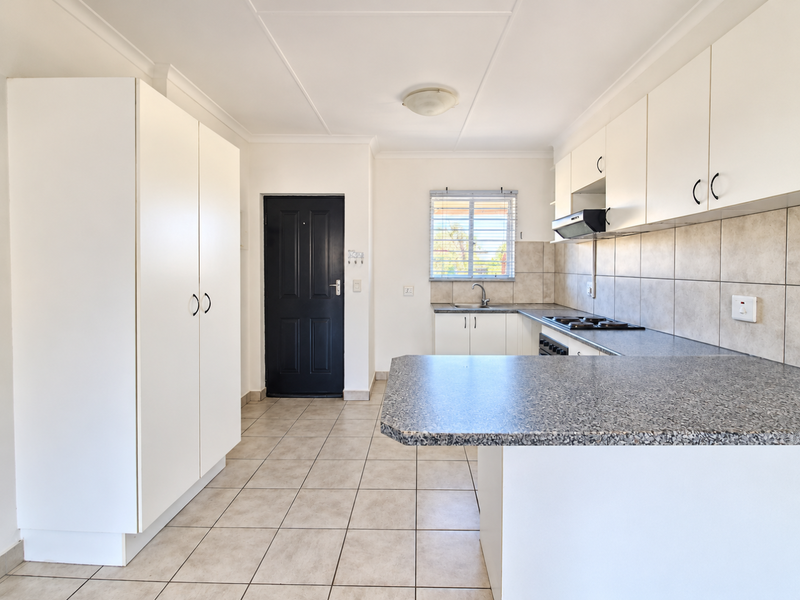 A clean, functional kitchen featuring white built-in cabinetry, granite-look laminate countertops, a tiled backsplash, and tiled flooring, offering a bright and well-maintained workspace.