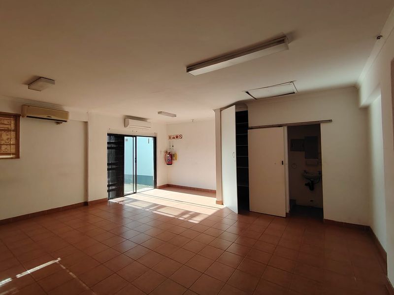 Spacious empty office area featuring tiled flooring, built-in storage, air conditioning units, and direct access to an outdoor area.