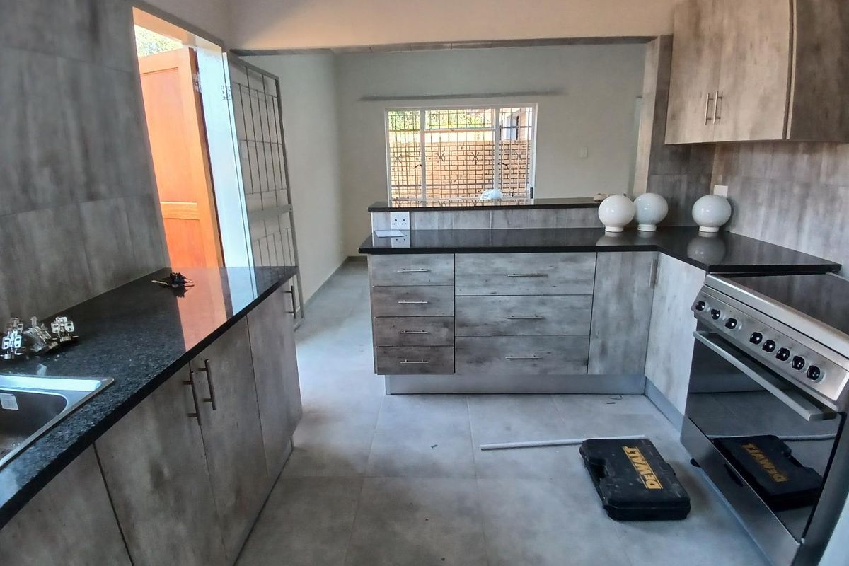 Modern kitchen featuring granite countertops, built-in cabinetry, and a stainless steel oven, with an open-plan layout leading to an exterior doorway.