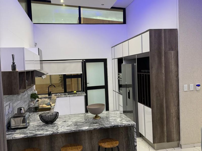 Modern kitchen featuring high-gloss cabinetry, stone countertops, integrated appliances, and a striking bulkhead with ambient blue lighting.