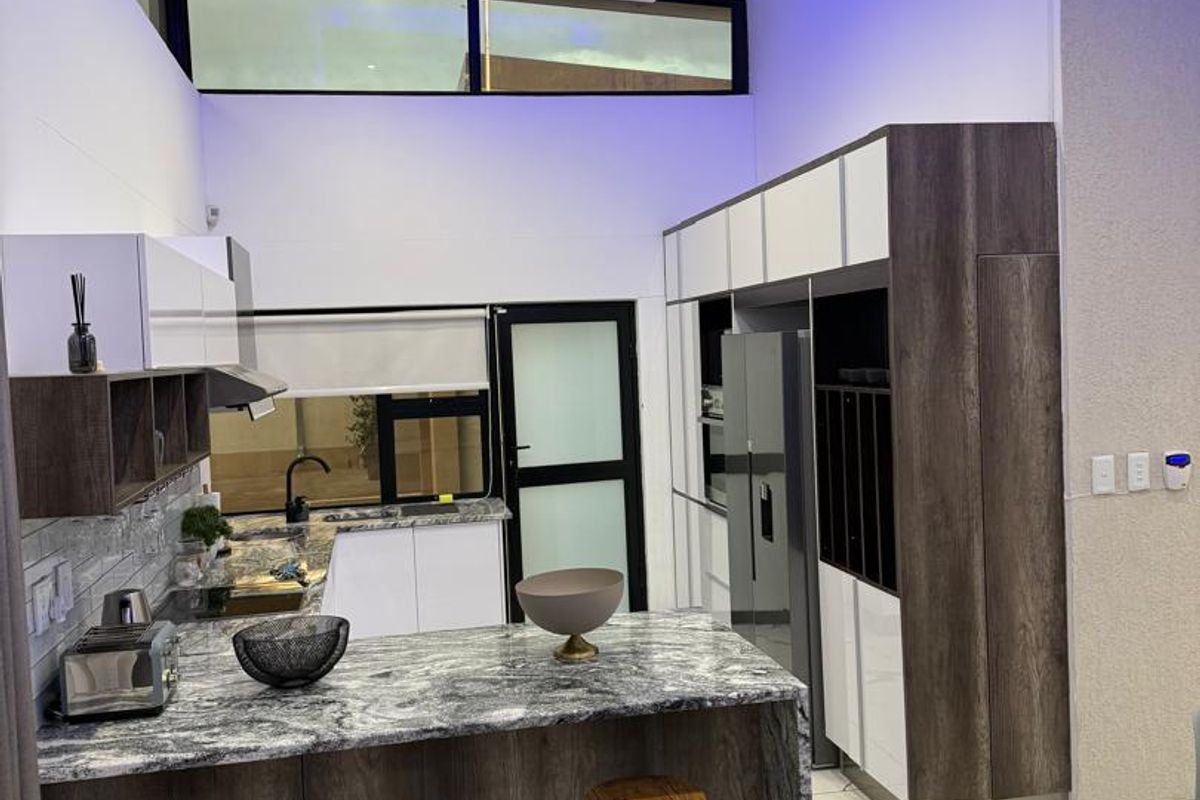 Modern kitchen featuring high-gloss cabinetry, stone countertops, integrated appliances, and a striking bulkhead with ambient blue lighting.
