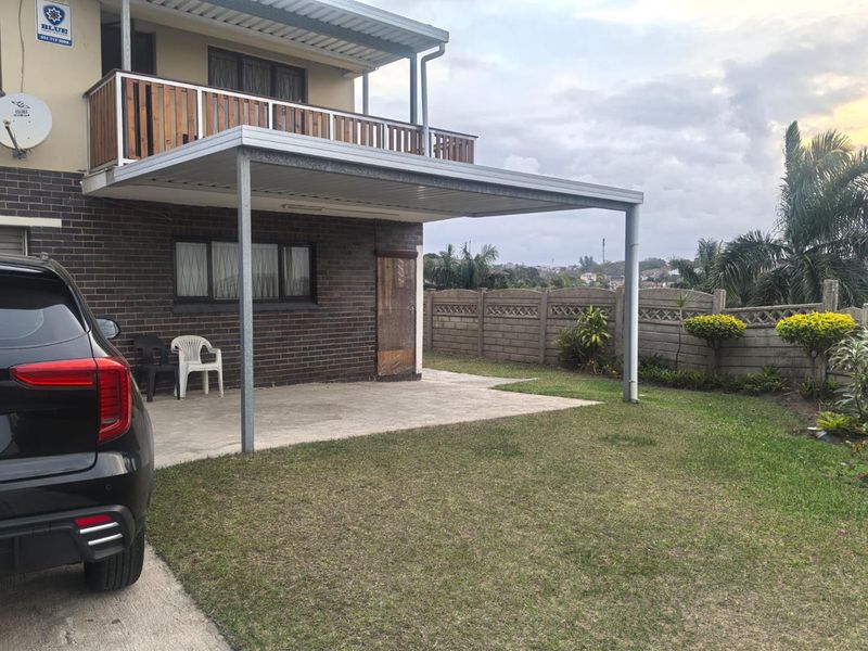 Rear view of the property featuring a covered patio area, an upper-level balcony with wooden railing, and a private garden with boundary walling.