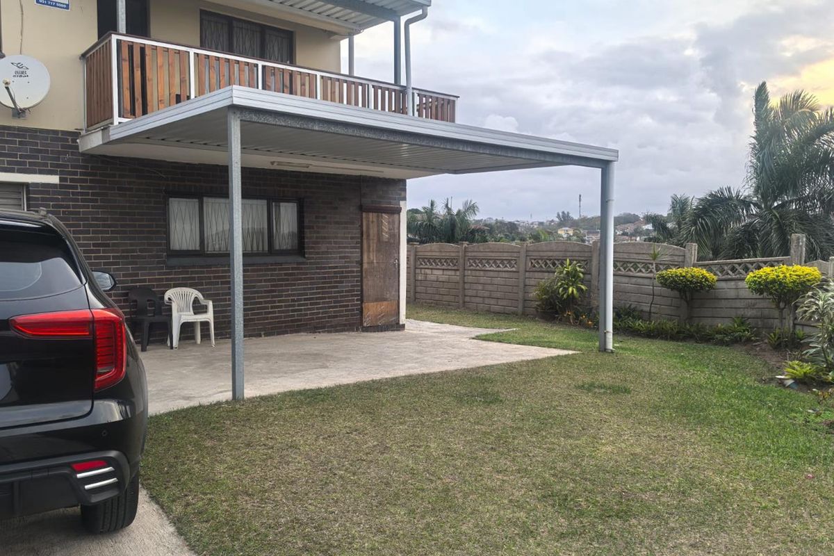 Rear view of the property featuring a covered patio area, an upper-level balcony with wooden railing, and a private garden with boundary walling.