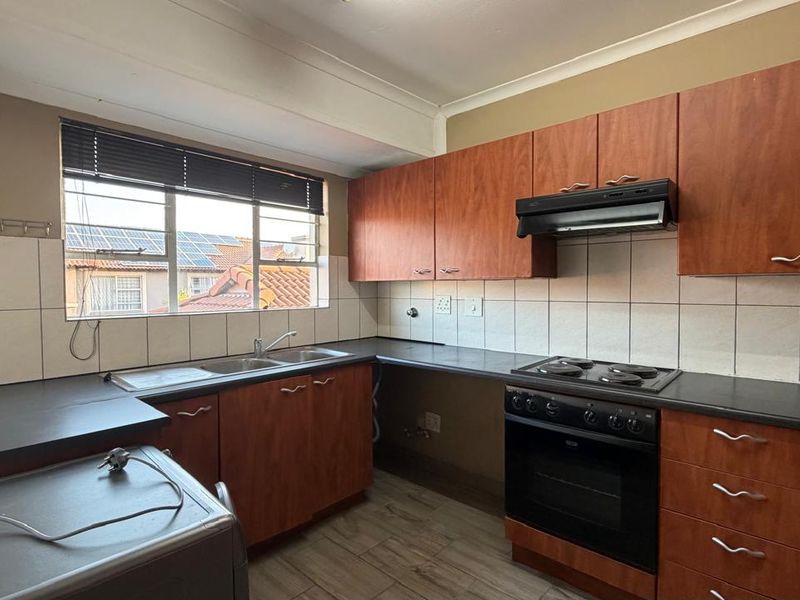 A functional kitchen featuring wood-look laminate cabinetry, dark countertops, a built-in oven with hob, and a double basin sink with tiled backsplash.