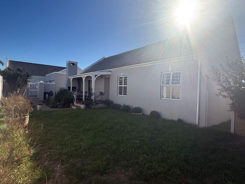 Rear view of the house featuring a covered patio with a built-in braai, overlooking a private garden area.