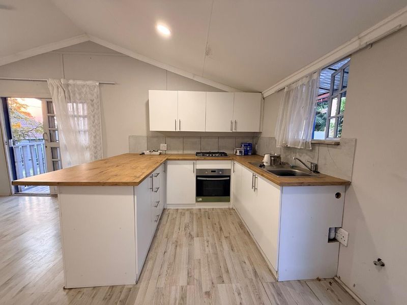 A functional kitchen featuring white cabinetry, wooden countertops, a gas hob, and an integrated oven, set within a space with a vaulted ceiling.