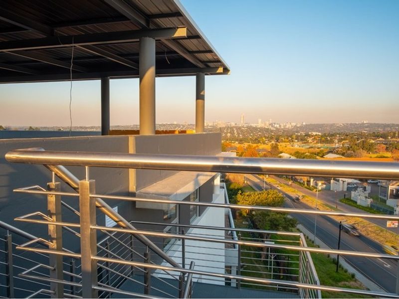 A modern covered balcony featuring a stainless steel balustrade and expansive elevated views of the surrounding cityscape.